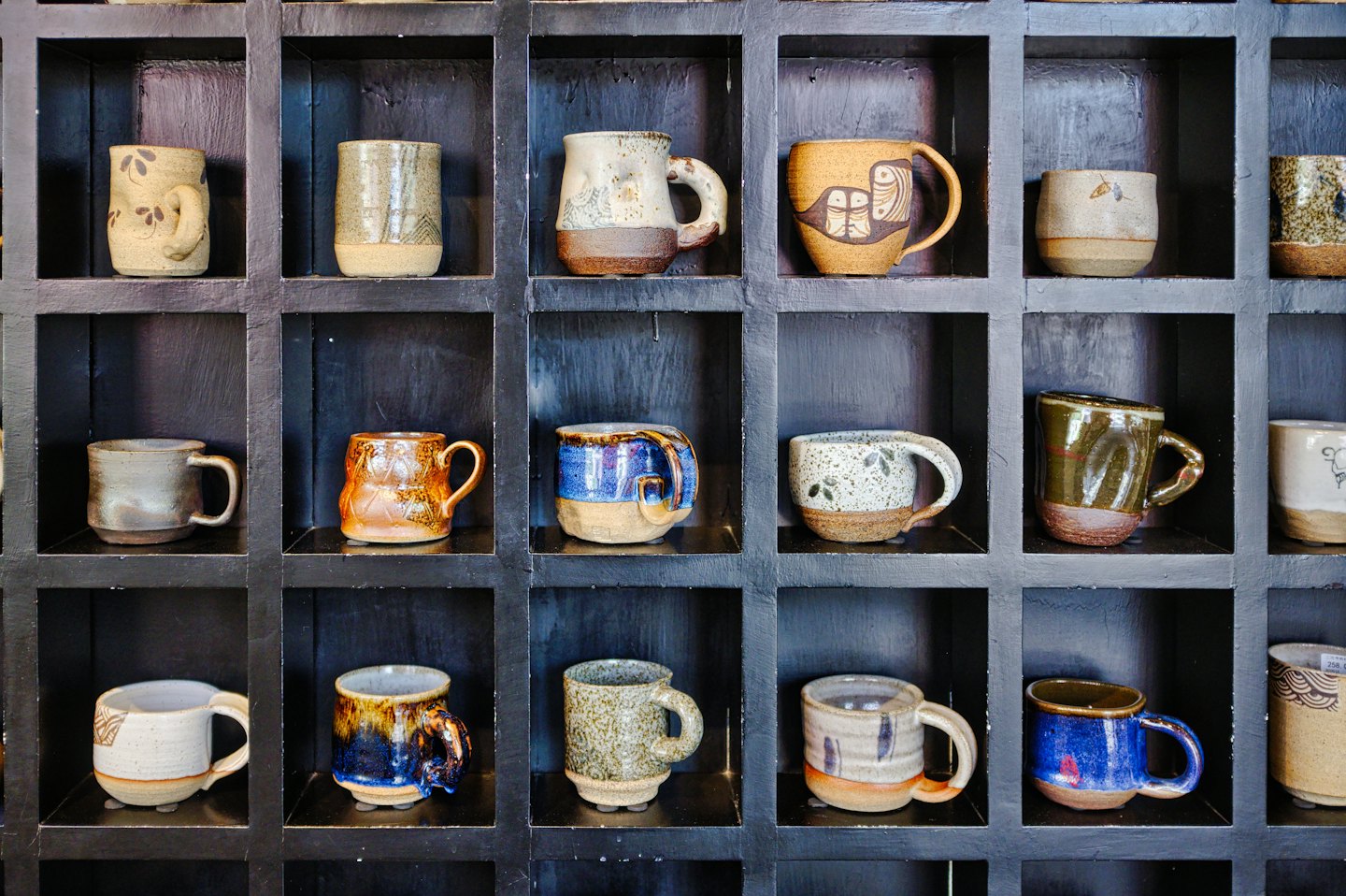 Ręcznie robione kubki ceramiczne na drewnianej półce.