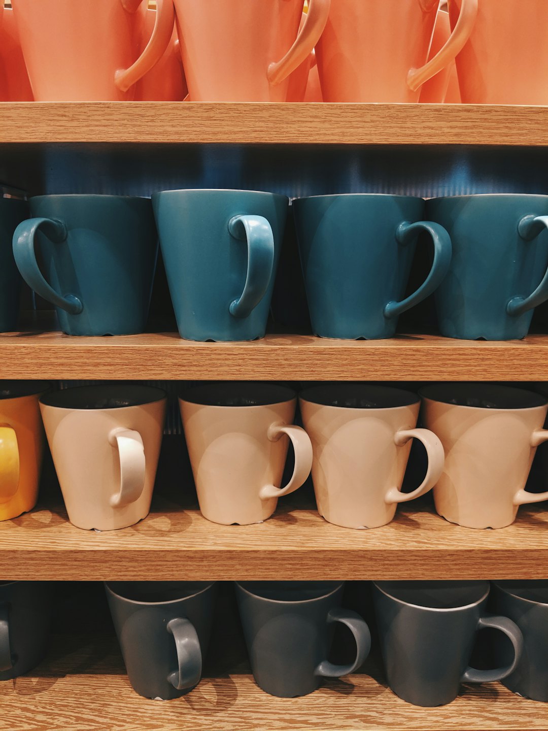 Kolorowe ceramiczne kubki ułożone na drewnianych półkach.